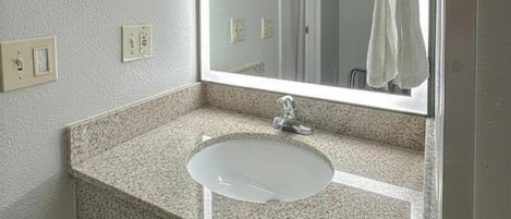 Un baño con encimera de granito, un lavamanos blanco y un espejo encima.