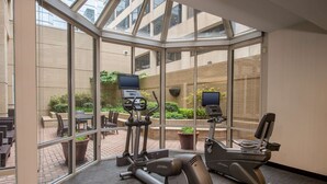Un gimnasio con equipo de ejercicio, ventanas amplias y vistas al patio exterior.