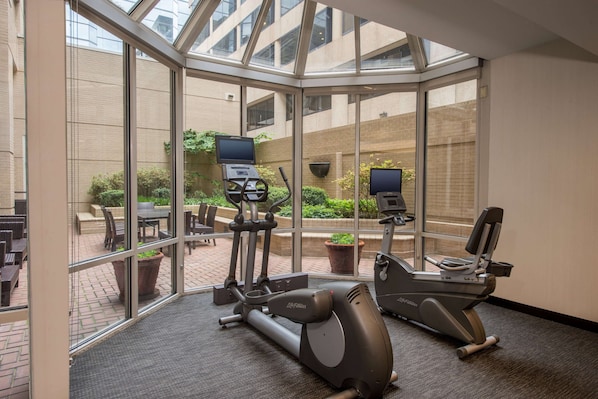 A gym with exercise equipment, large windows, and a view of the outside courtyard.
