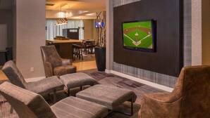 Una sala de estar moderna con un televisor de pantalla plana montado en la pared, una zona de comedor con barra, y un área de descanso con sofás y sillones.