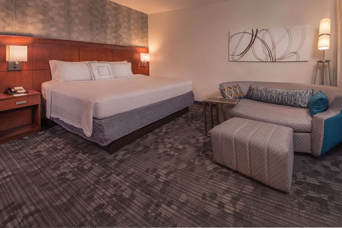 A hotel room with a large bed, a sofa, a small table, and a lamp.