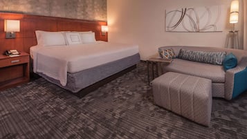 A hotel room with a large bed, a sofa, a small table, and a lamp.