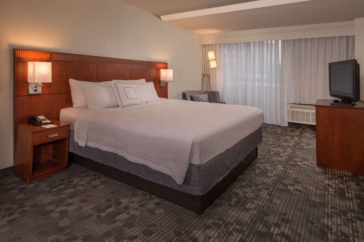 A hotel room with a large bed, two bedside lamps, a desk with a television, and a window with curtains.