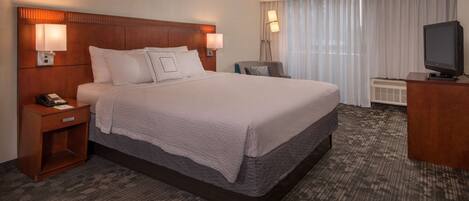 A hotel room with a large bed, two bedside lamps, a desk with a television, and a window with curtains.