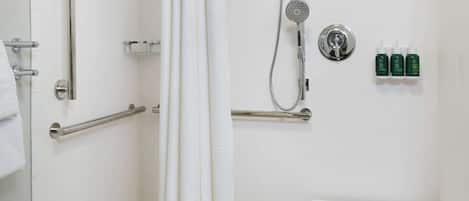 A modern bathroom with a walk-in shower, grab bars, a white sink, and a small table.