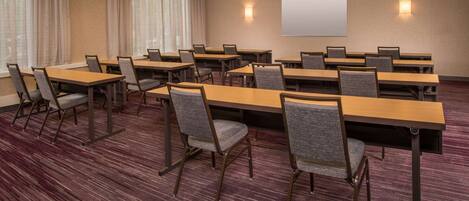 A conference room with tables and chairs, a projector screen, and a carpeted floor.