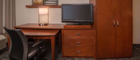 A hotel room with a wooden desk, a television, a lamp, a chair, and a wardrobe.