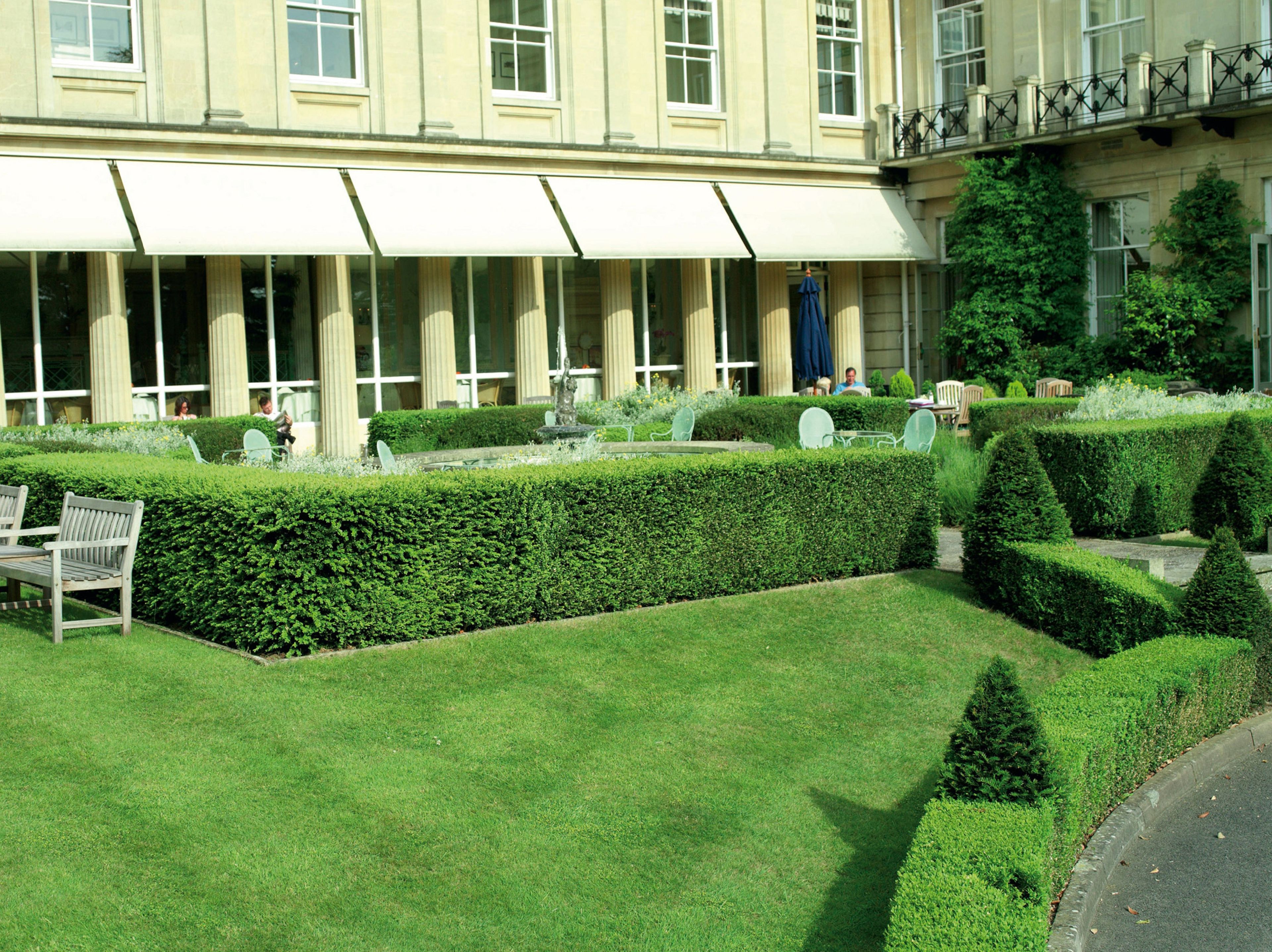 A courtyard with neatly trimmed hedges, a bench, and outdoor seating.