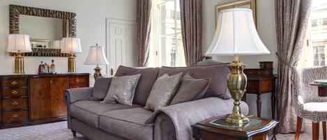 A well-lit room with a large sofa, two lamps, a mirror, and a wooden dresser.