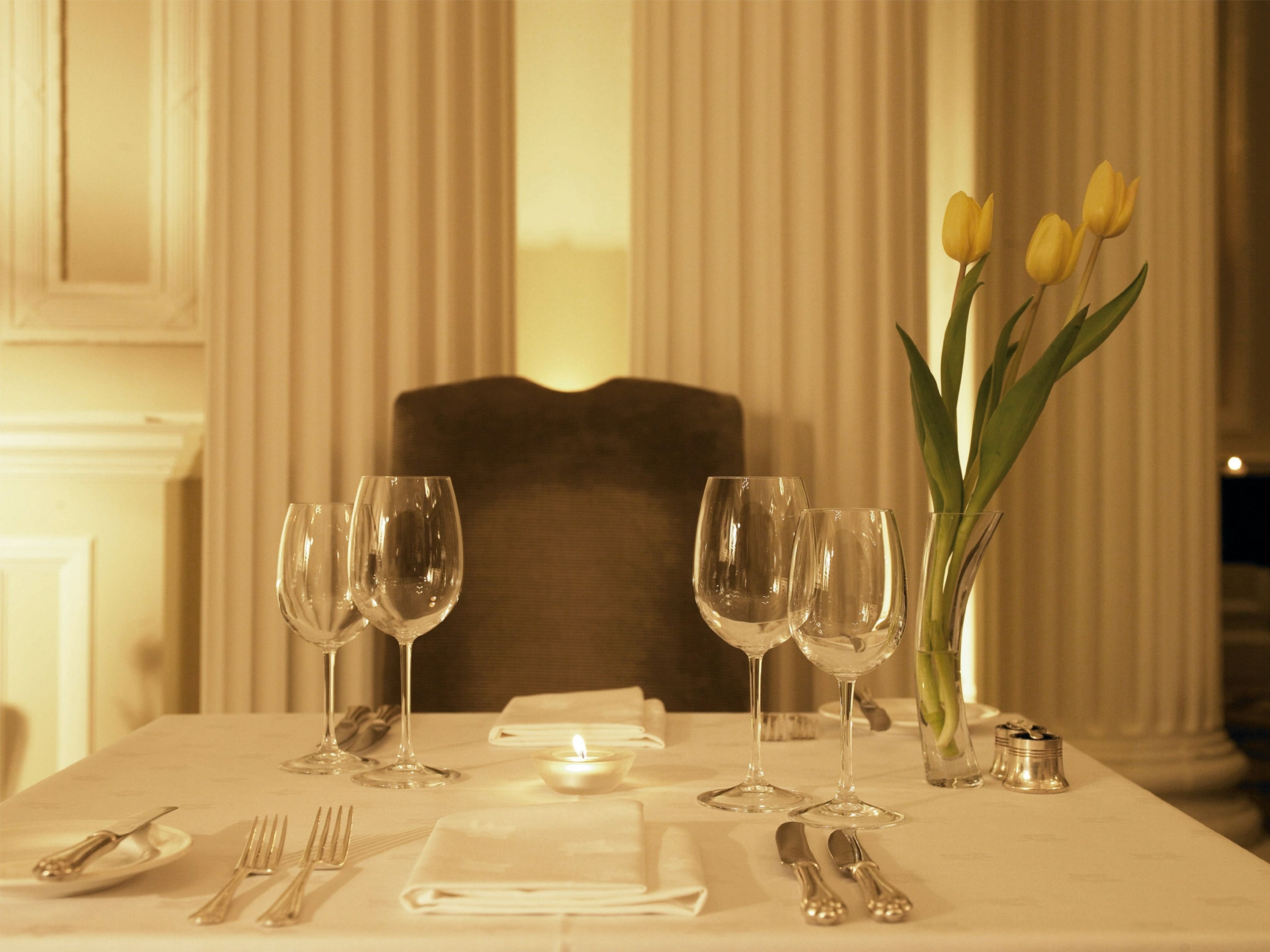 A dining table set with wine glasses, a candle, and a vase with yellow tulips.