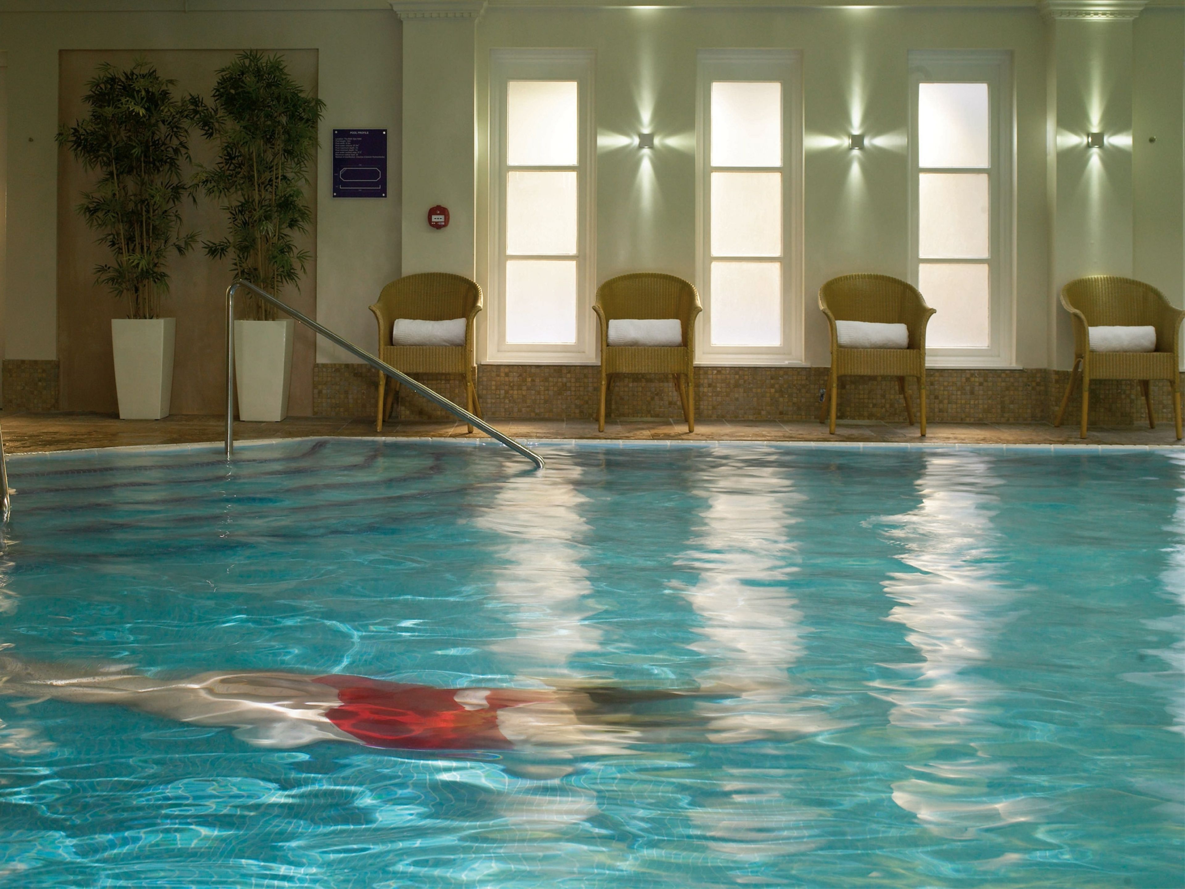 Une piscine intérieure à l’eau claire, entourée de fauteuils en osier avec des coussins blancs.