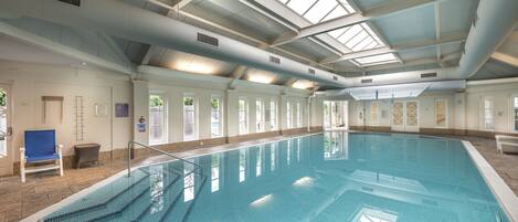 Una piscina interior con agua cristalina azul, suelo de baldosas y techo alto con tragaluces.