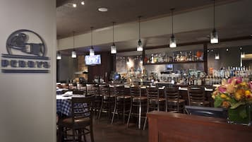 A bar area with multiple seating arrangements, a television screen, and a variety of bottles on shelves.