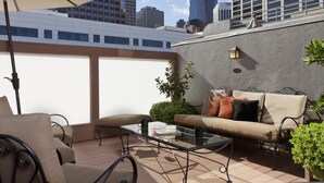 A rooftop patio with a glass table, a sofa, and an umbrella.