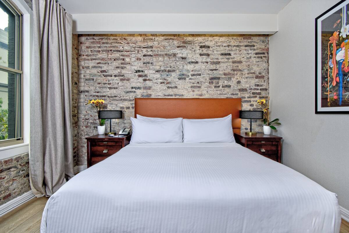 A neatly made bed with white linens, a brick-patterned headboard, and two bedside tables with lamps and vases.