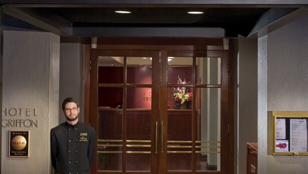 A hotel entrance with a double door, a doormat, and a sign above the door.