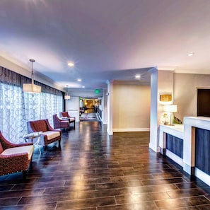 A hotel lobby with a reception desk, seating area with chairs, and a hallway leading to other rooms.
