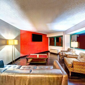 A modern living room with a red accent wall, leather sofa, patterned armchairs, a glass coffee table, and a flat-screen TV mounted on the wall. - Holiday Inn Princeton by IHG (Princeton)