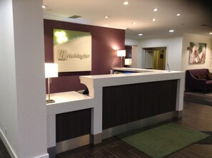 A reception desk with a sign above it, a lamp, and a couch in the background. - Holiday Inn Princeton by IHG (Princeton)