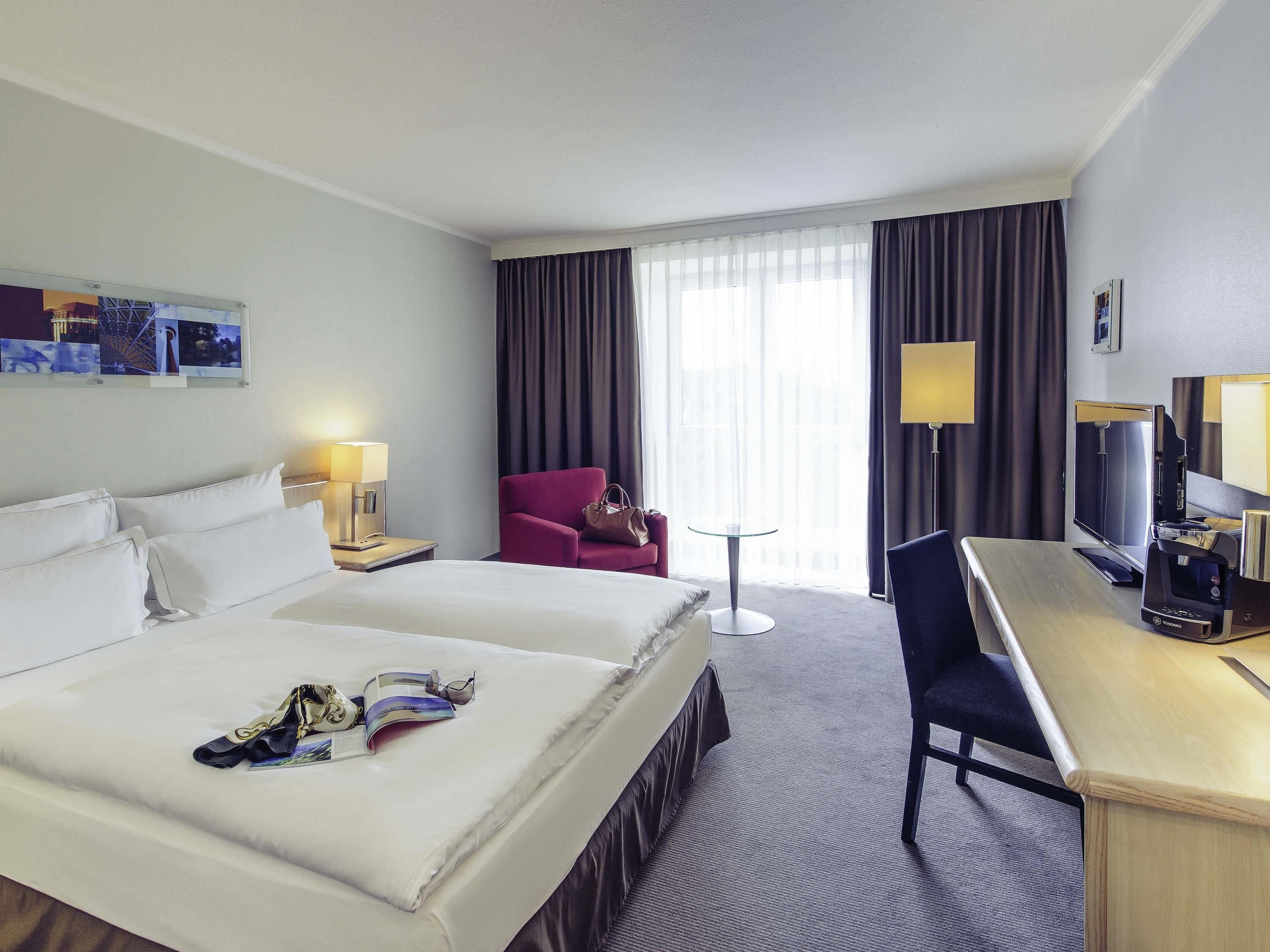 A hotel room with a bed, a desk, a chair, a TV, and a window with curtains.