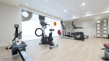 A modern gym with cardio machines, a rowing machine, and a wall-mounted TV.