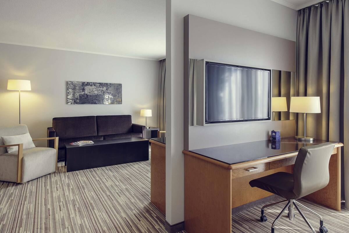 Une chambre d’hôtel équipée d’un lit, d’un bureau, d’une chaise, d’une télévision et de deux lampes.