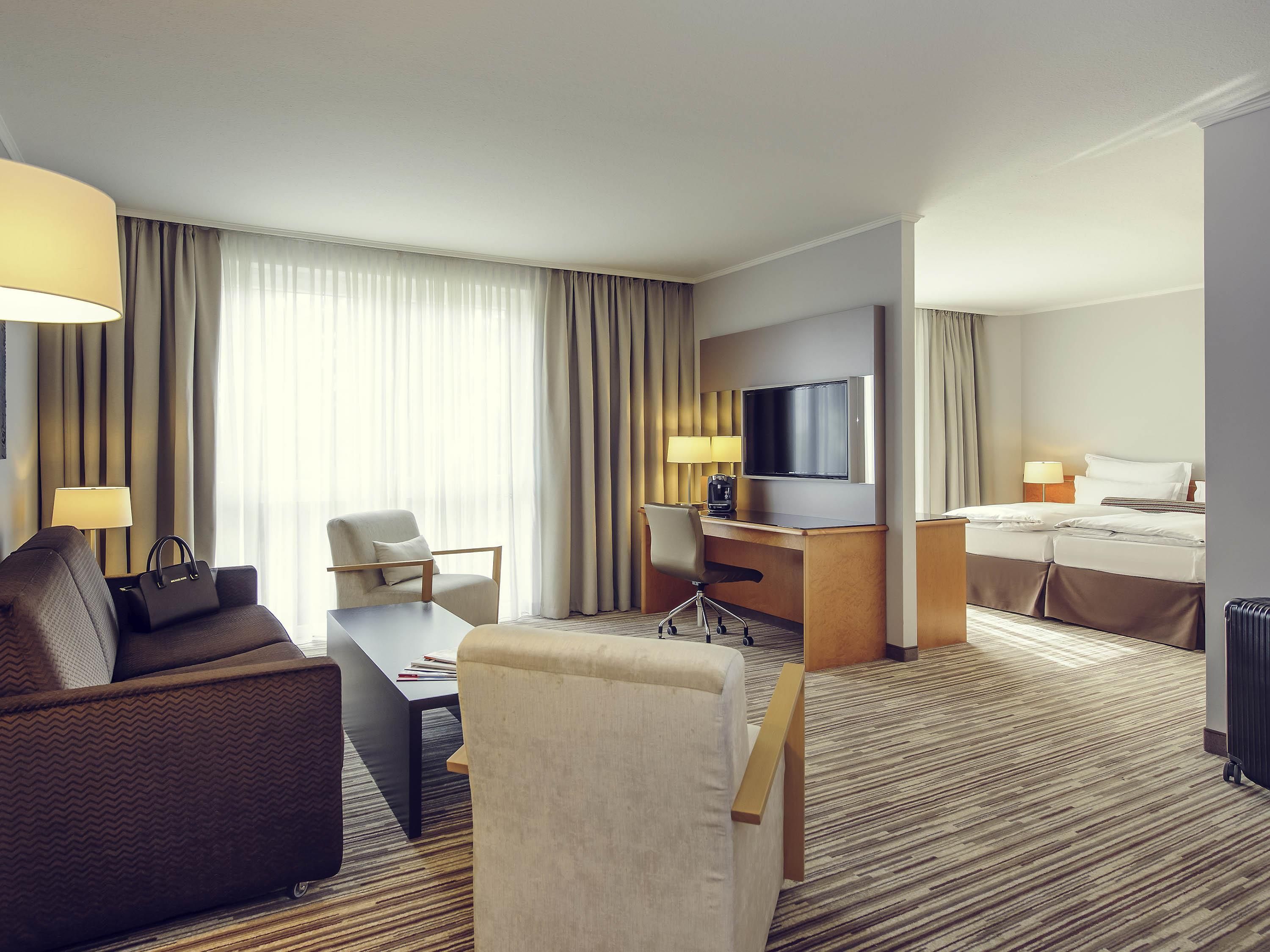A hotel room with a sofa, desk, chair, bed, TV, and a view of the outdoors.