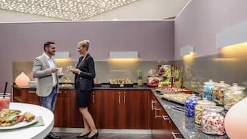 Un hall d’hôtel moderne avec un présentoir de nourriture, des meubles en bois et un plafond orné de luminaires circulaires.