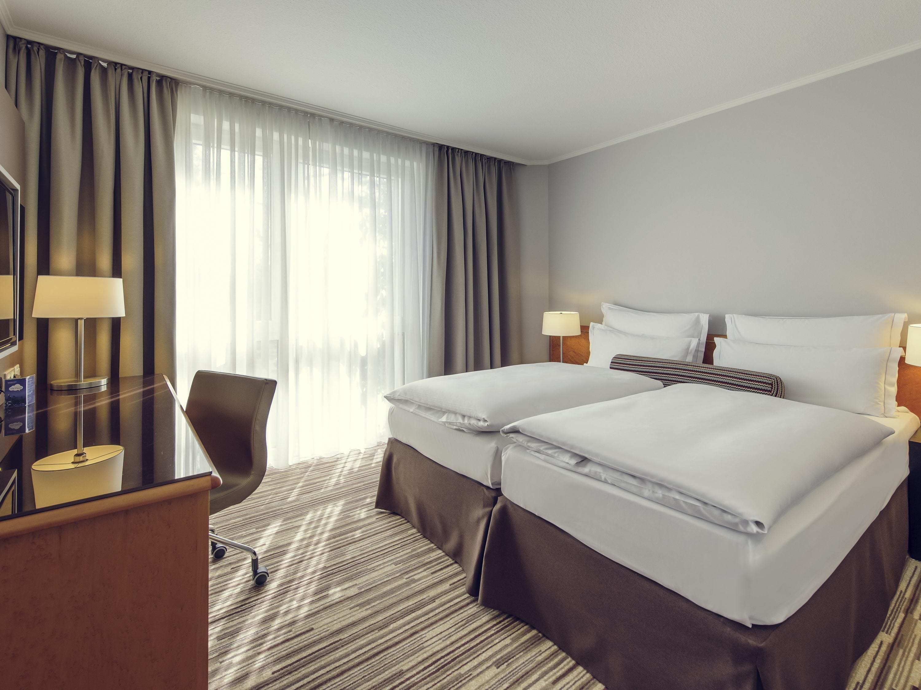 A hotel room with two beds, a desk, a chair, and a TV.