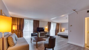 A modern hotel room with a sofa, armchair, desk, and television. - Mercure Hotel Düsseldorf Kaarst (Kaarst)