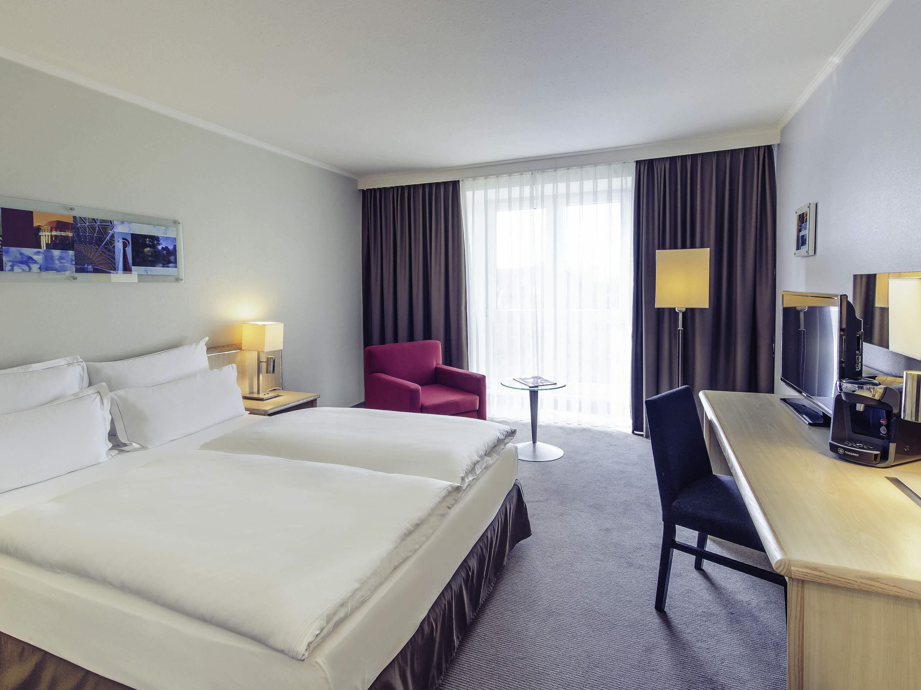 Une chambre d’hôtel avec un grand lit, un bureau avec un ordinateur, une chaise, une petite table et un téléviseur.