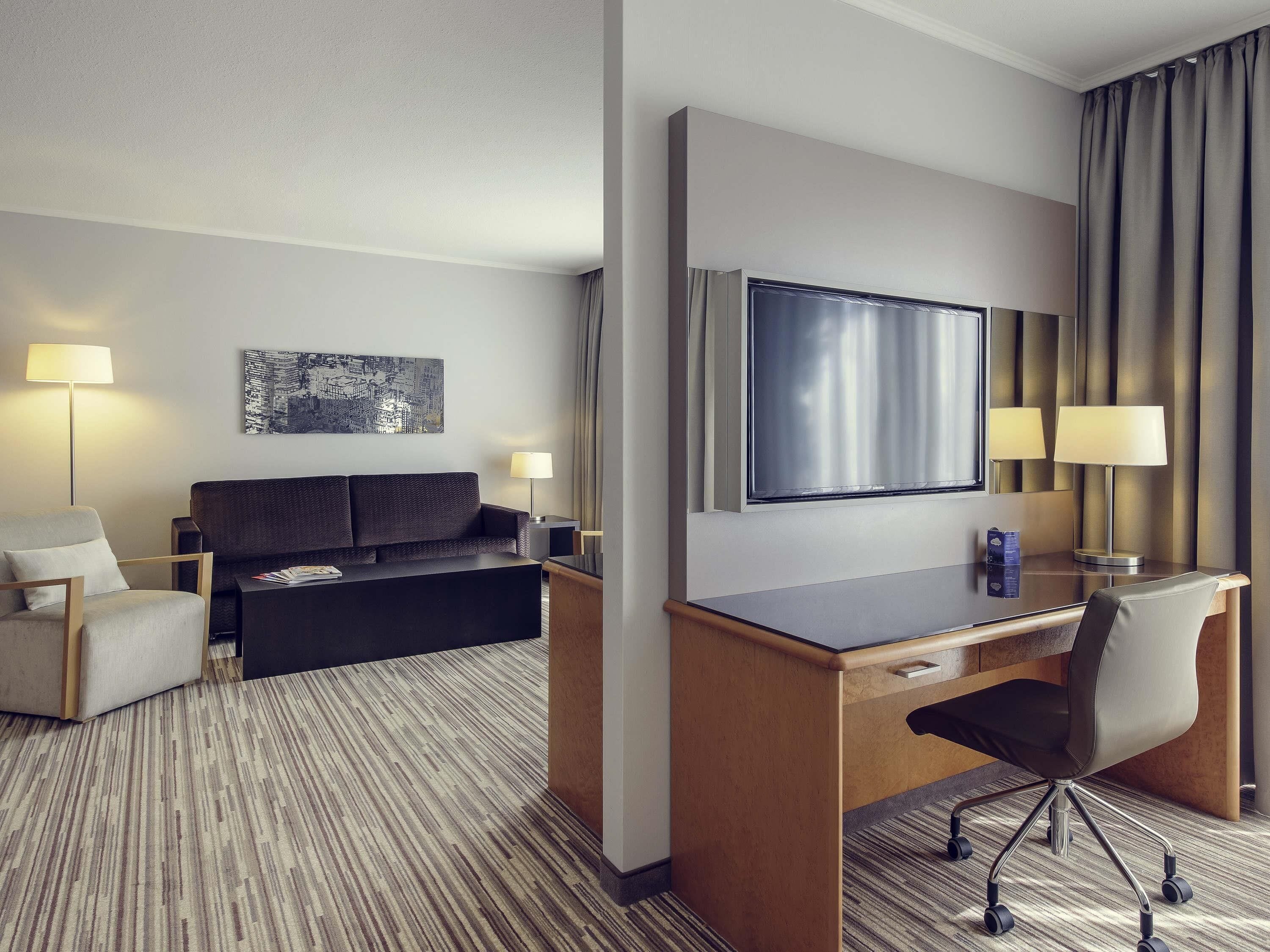 Une chambre d’hôtel équipée d’un lit, d’un bureau, d’une chaise, d’une télévision et de deux lampes.