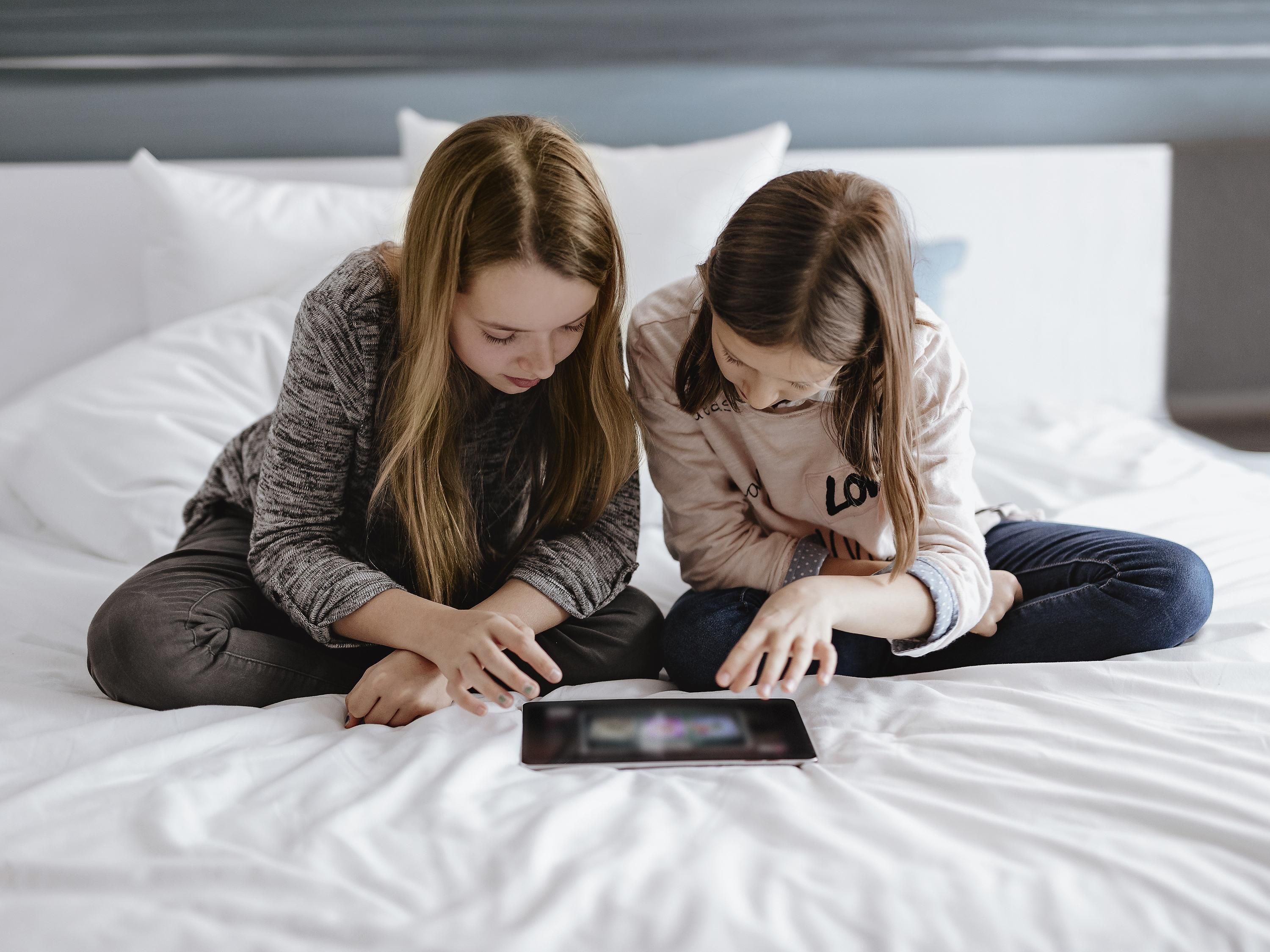 Two individuals sitting on a bed with a tablet in front of them.