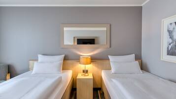 Une chambre d’hôtel avec deux lits, une table de chevet avec une lampe, un tableau encadré au mur et un tapis à rayures.