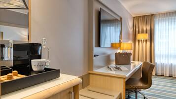 A hotel room with a desk, chair, coffee maker, and a mirror.