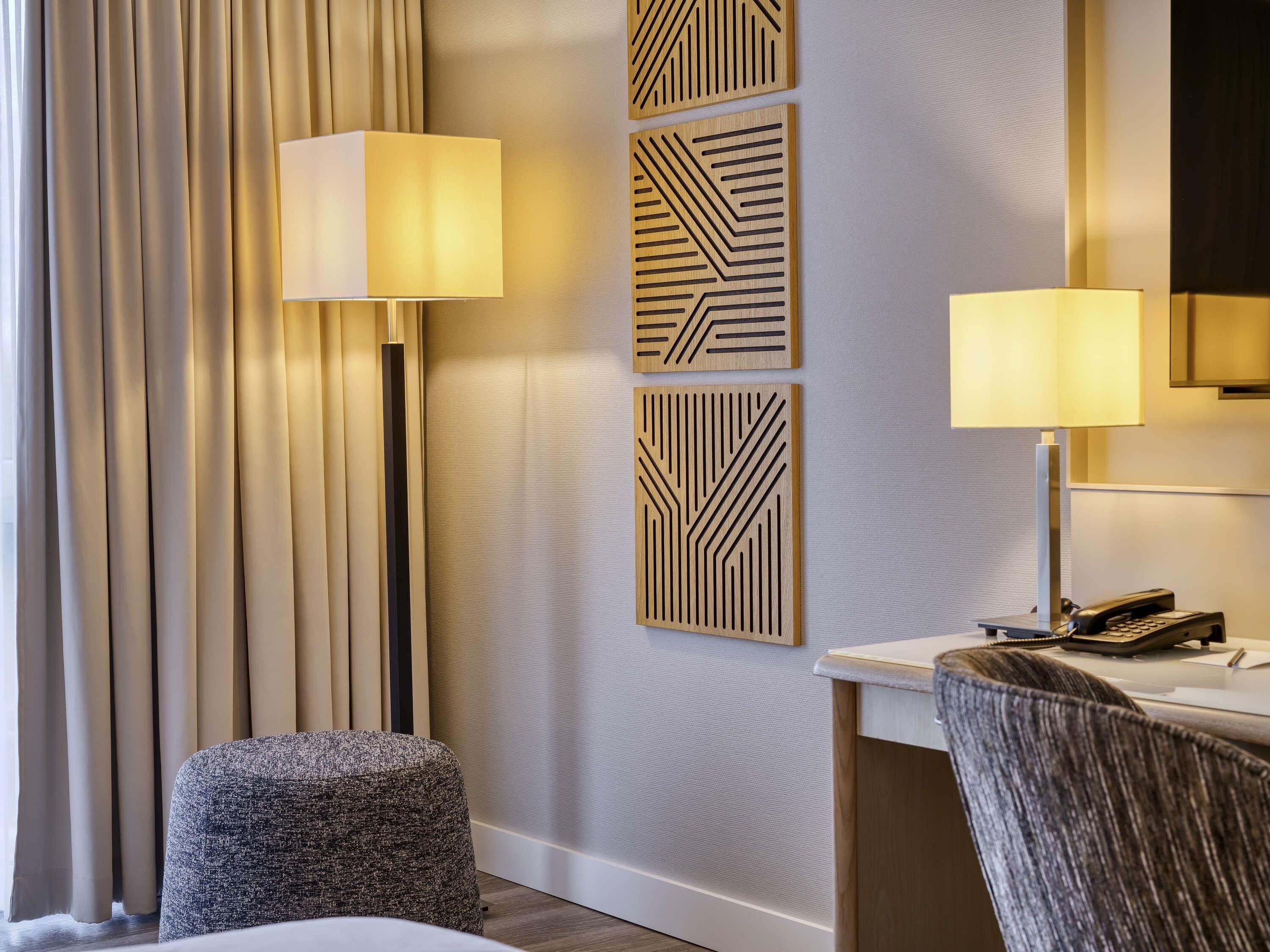 A hotel room with a bed, a desk with a phone, a lamp, and a chair.