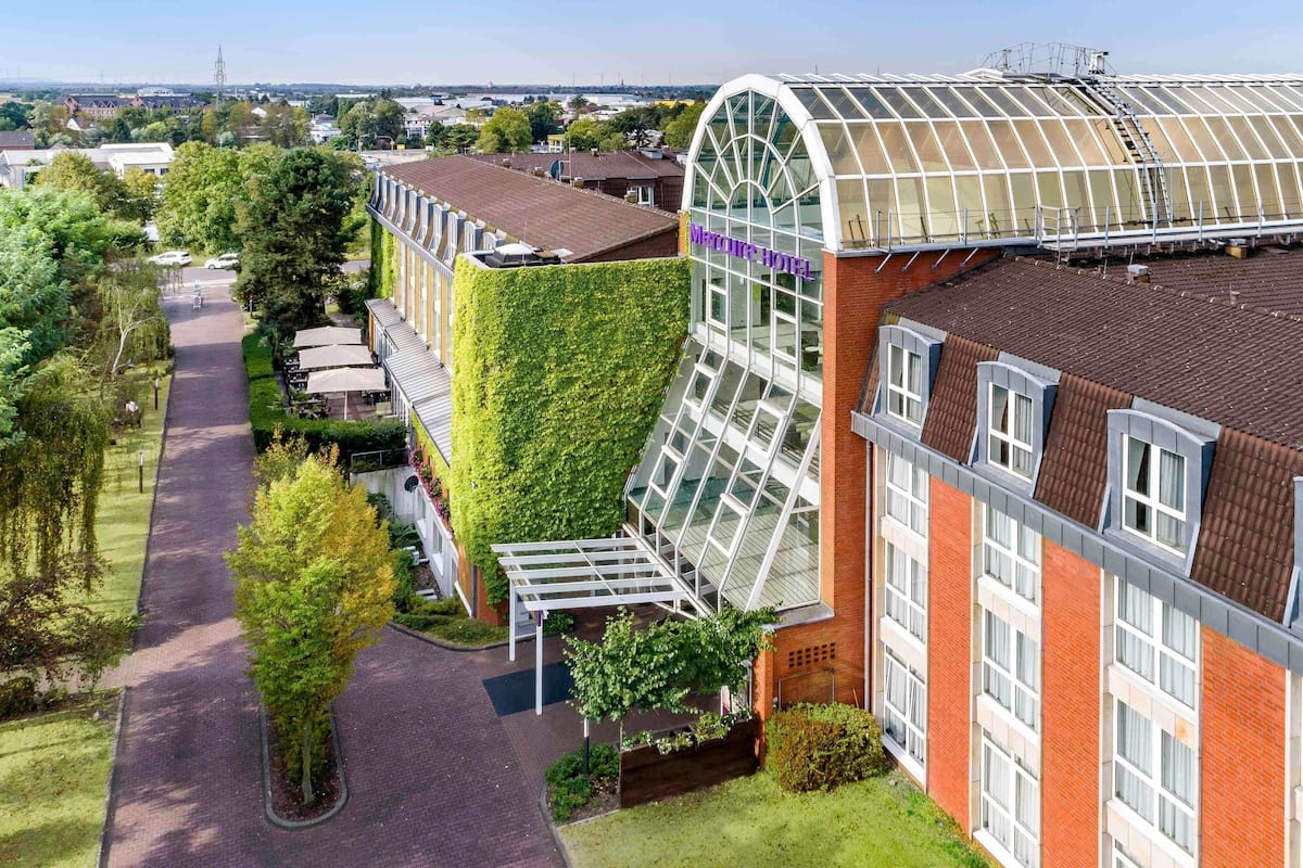 Un hôtel doté d’une façade en verre incurvé, d’un mur végétal et d’une galerie couverte.