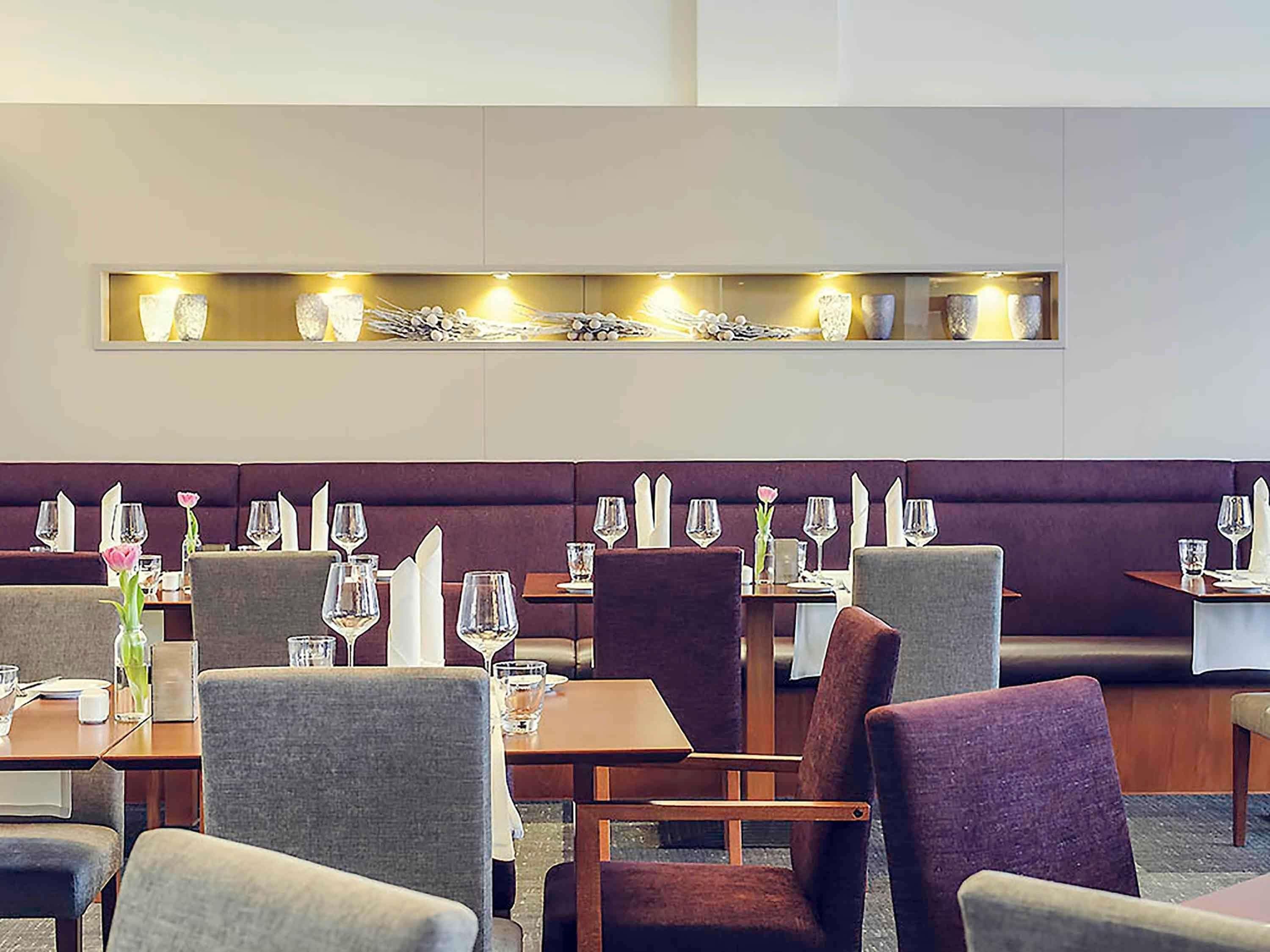 Un restaurante con una larga banqueta, mesas con sillas y un aplique en la pared.