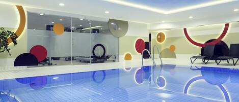 Una piscina interior moderna con baldosas azules brillantes, paredes de cristal y arte contemporáneo en las paredes.