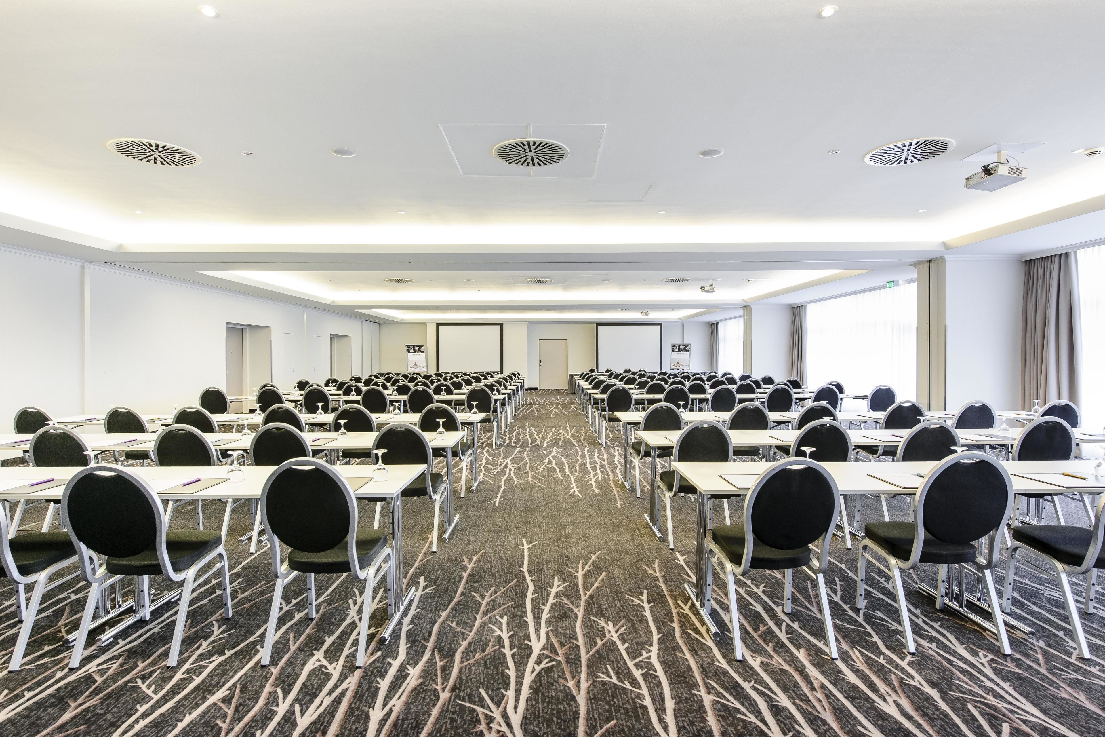 A conference room with rows of tables and chairs, a patterned carpet, and a modern ceiling design.