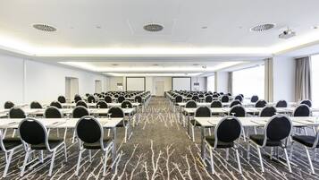 A conference room with rows of tables and chairs, a patterned carpet, and a modern ceiling design.