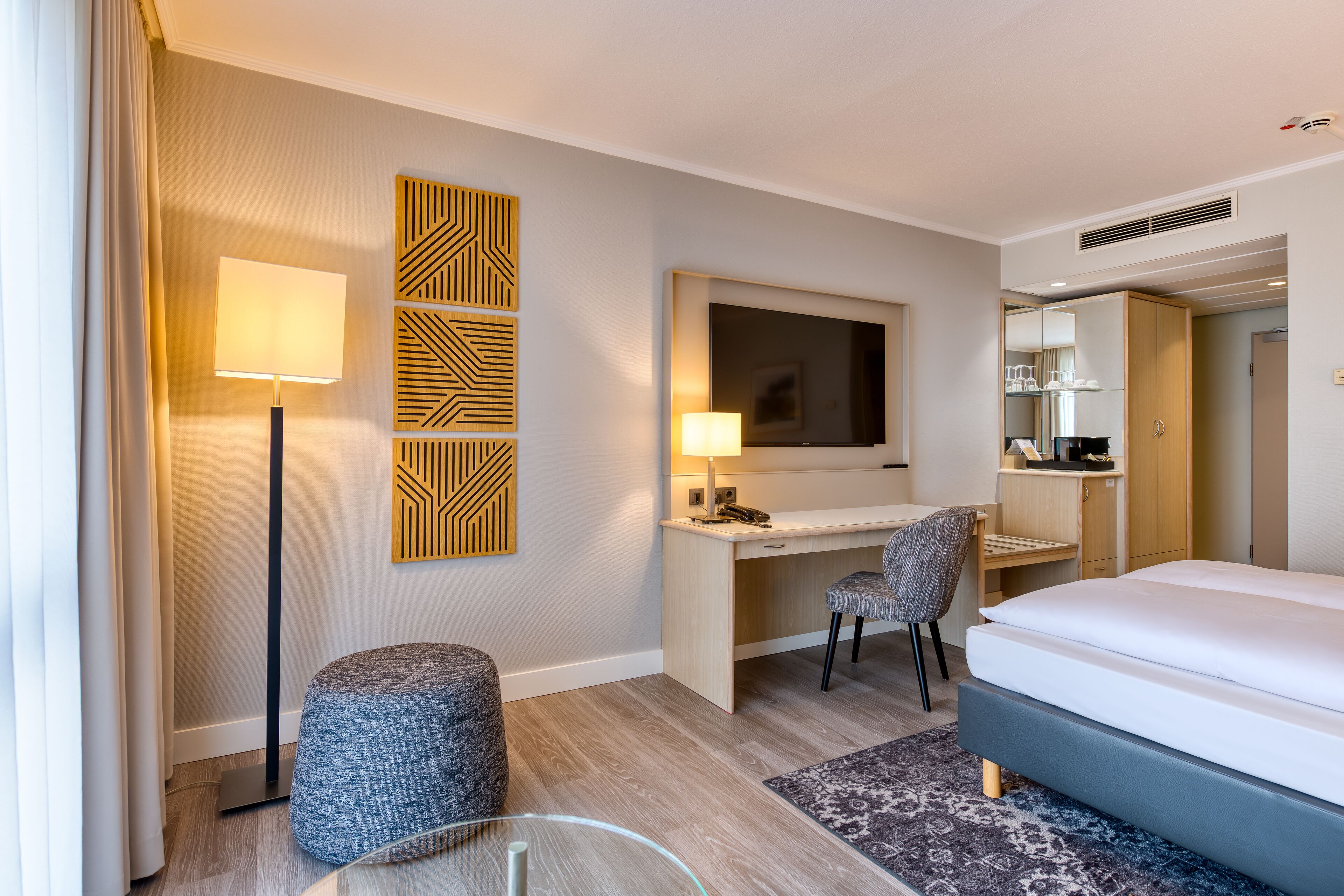 A hotel room with a bed, desk, chair, and a TV.