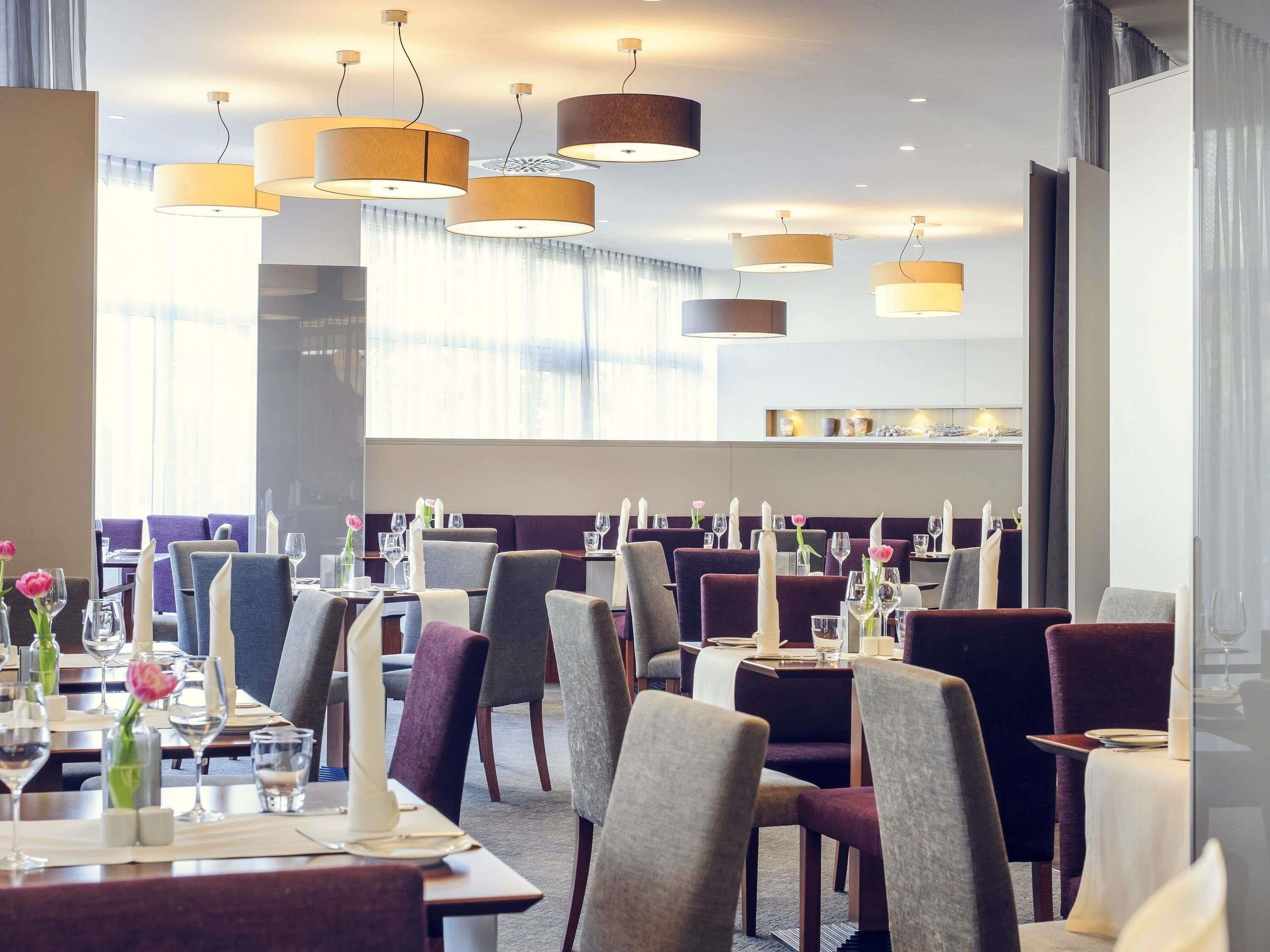 A restaurant with multiple tables, chairs, and hanging pendant lights.