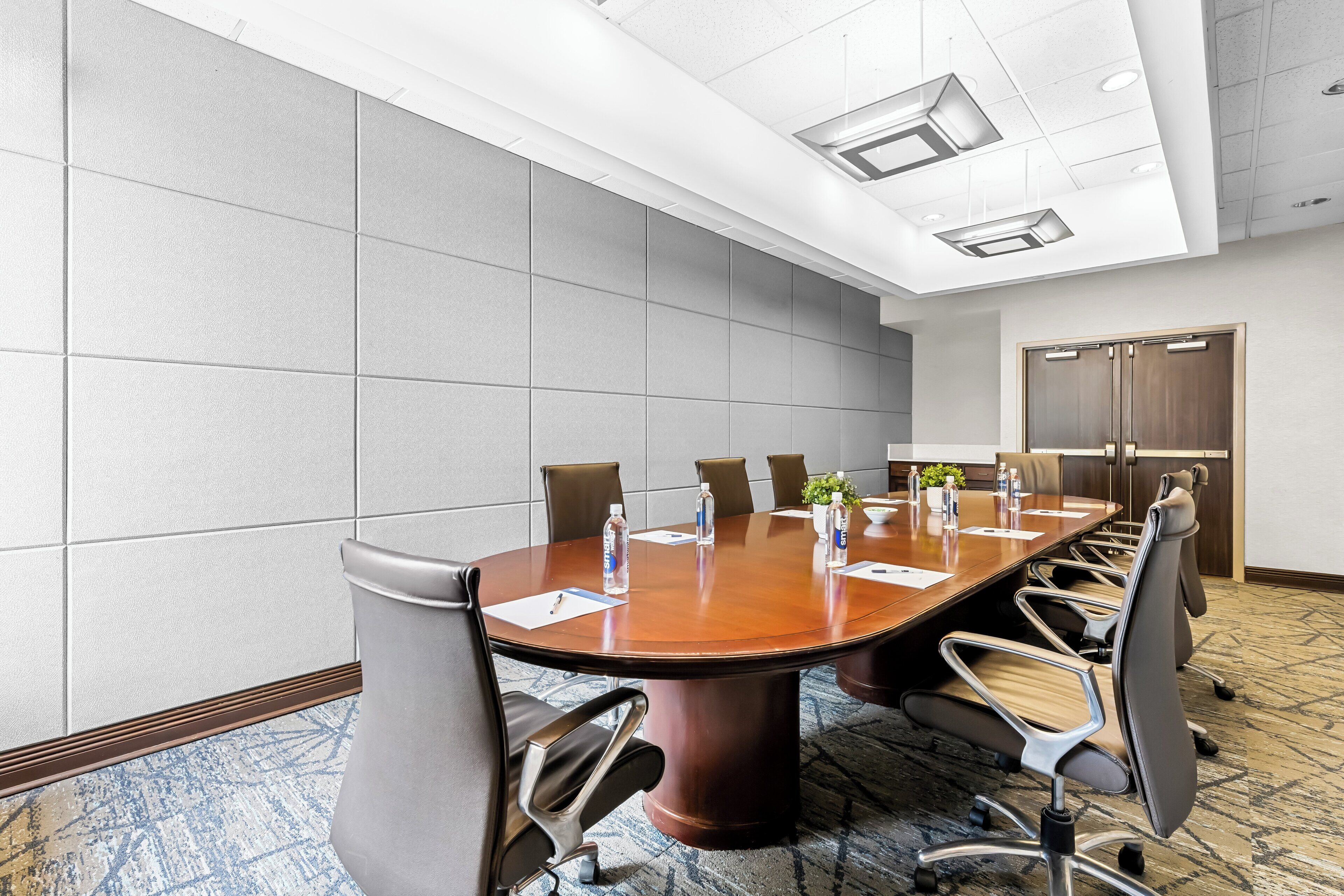 A conference room with a large oval table, six chairs, and a door in the background.