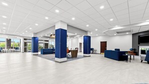 A spacious lobby with a modern design, featuring a reception desk, seating areas, and a large window providing a view of the outdoors.