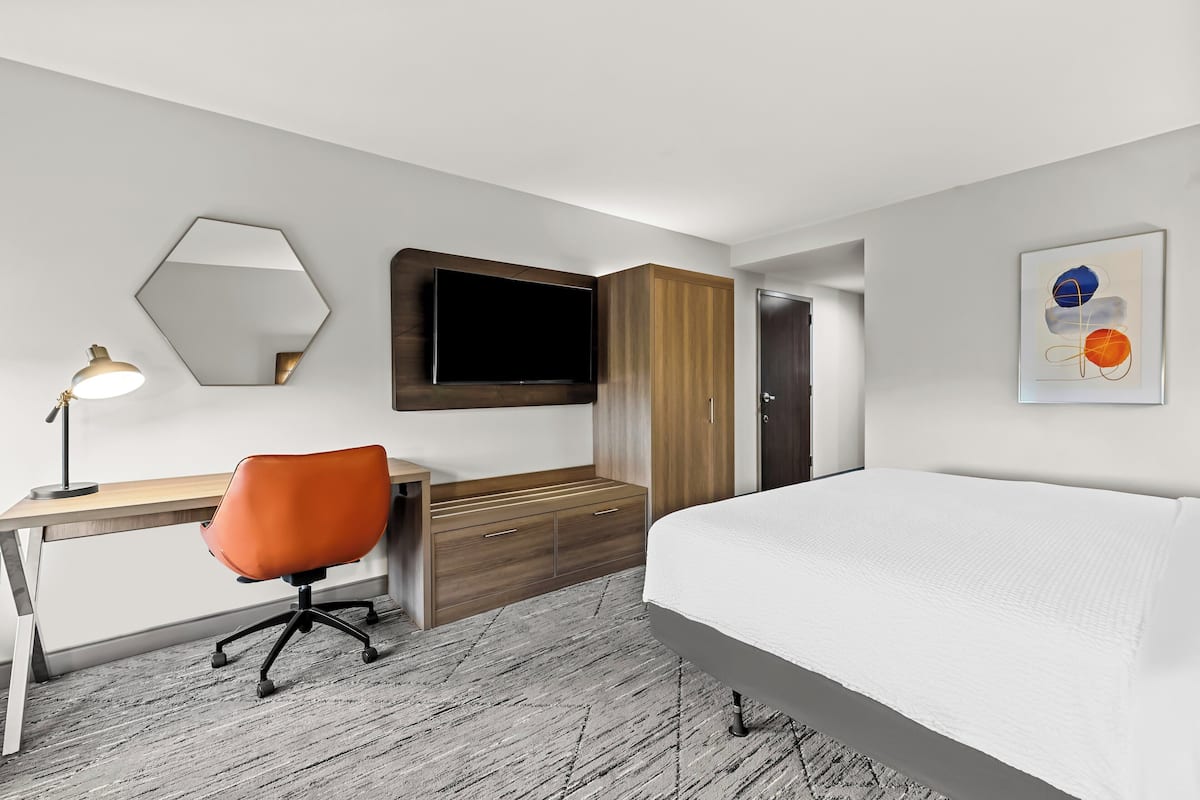 Une chambre d’hôtel moderne équipée d’un lit, d’un bureau, d’une chaise, d’une télévision, d’une armoire et d’œuvres d’art.