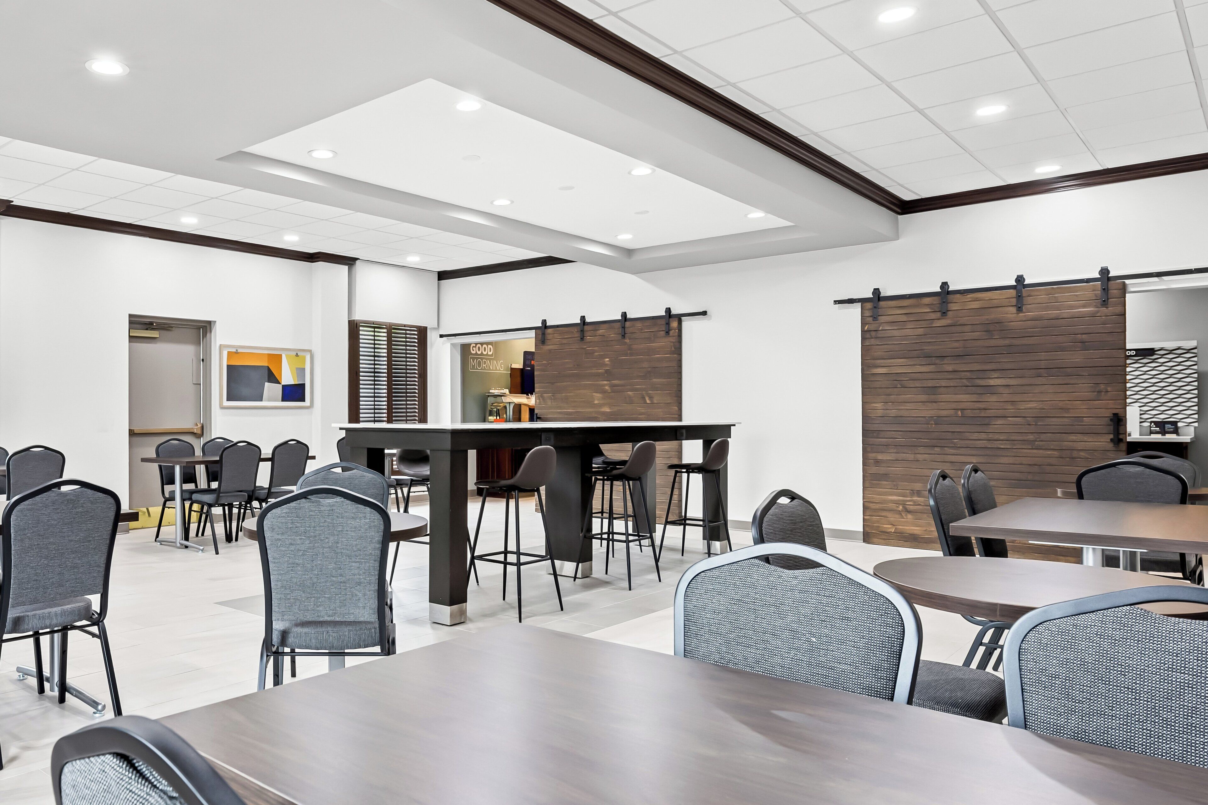 Una sala de conferencias moderna con una larga mesa y múltiples sillas, un área de cocina y una pared de acento de madera.