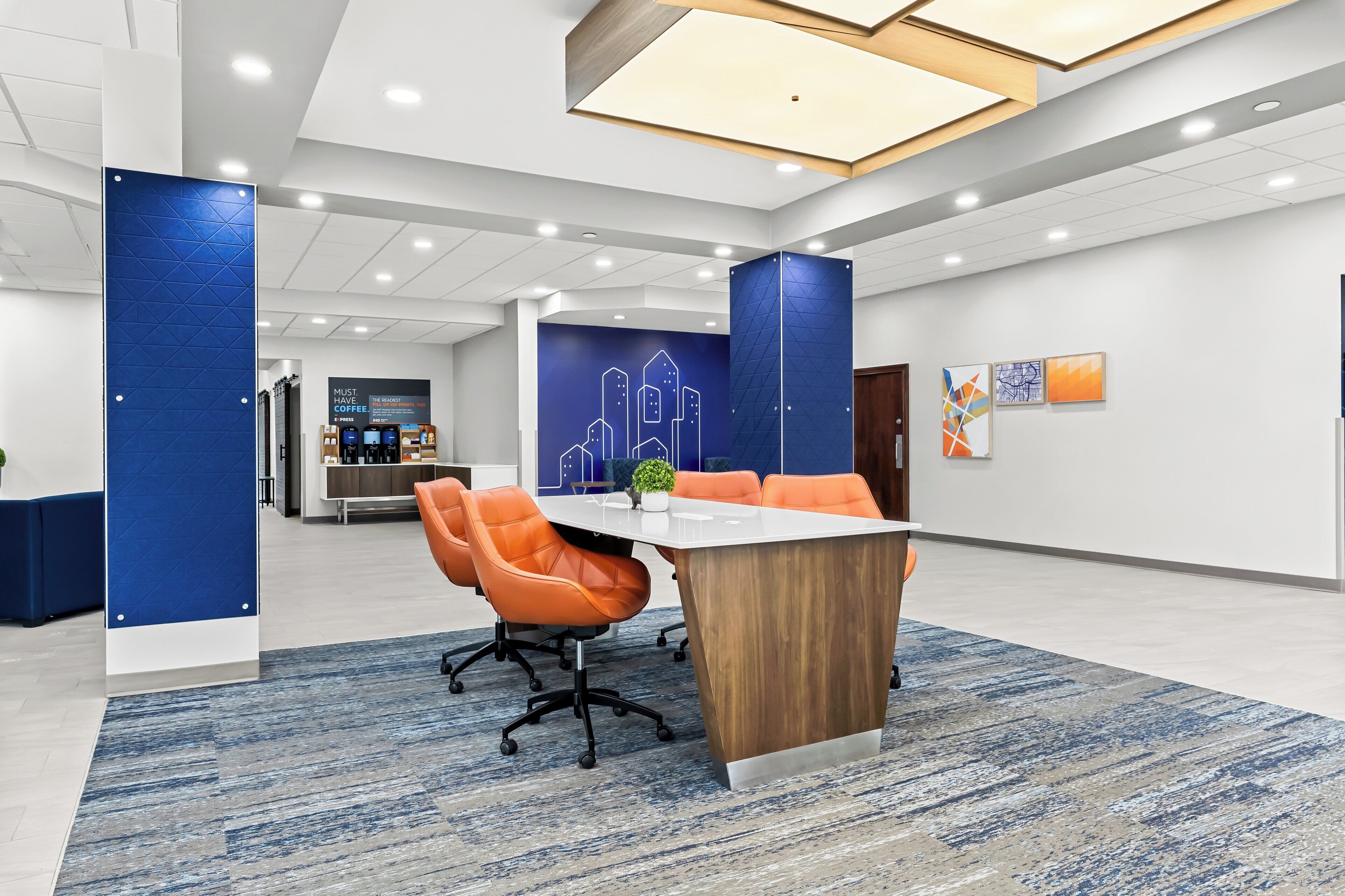 A modern conference room with a white table, orange chairs, and a blue accent wall with a cityscape design.
