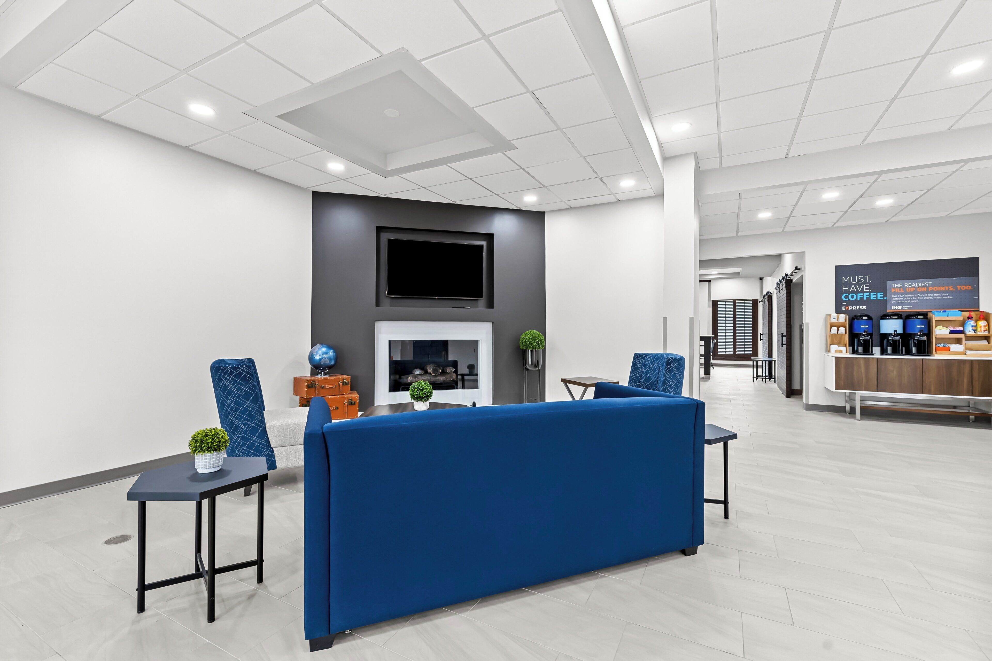 A modern lobby with a blue sofa, a fireplace, a TV, and a coffee station.