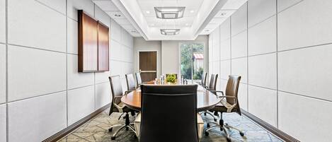 A conference room with a long table, chairs, and a view of a building through a window.